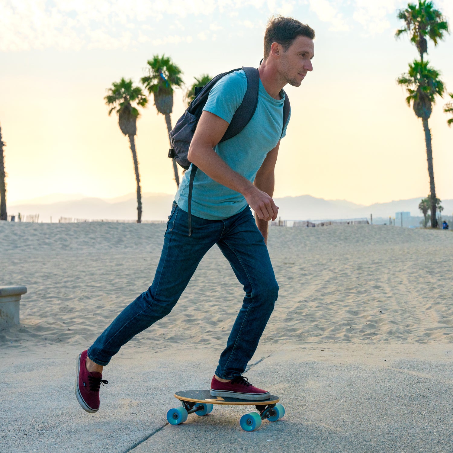 A guy riding an Eggboard mini cruiser skateboard with blue wheels at sunset by the beach. The warm colors of the setting sun create a stunning backdrop, emphasizing the skateboard's sleek design and the joy of cruising along the shoreline. This scene captures the essence of carefree summer evenings, perfect for beach adventures