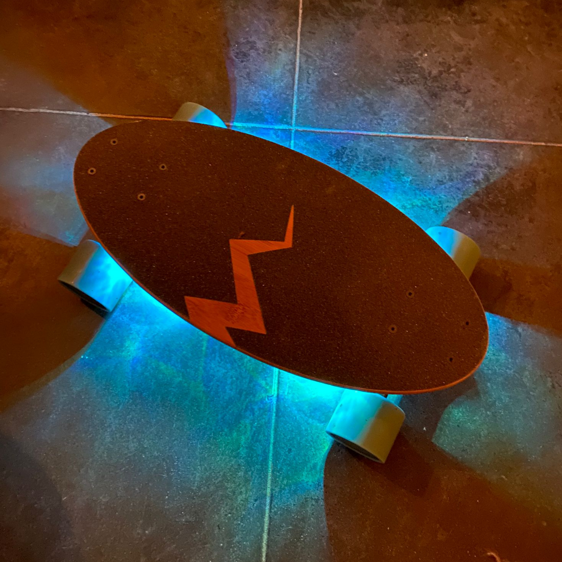 Top view of an Eggboard cruiser skateboard featuring blue underglow lights, showcasing the vibrant glow underneath, highlighting the board's design and functionality.