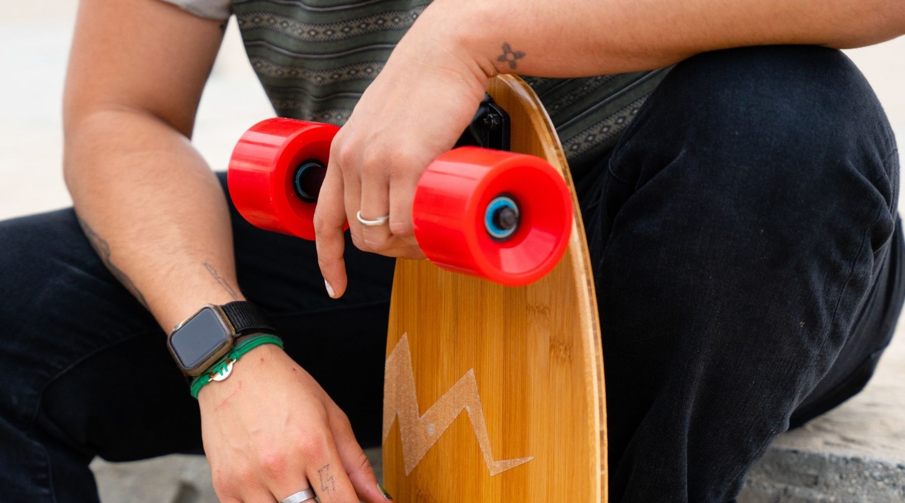 Closeup of a guy sitting and resting his hand on an Eggboard mini cruiser skateboard held up near his leg, emphasizing the board's sleek design and personal connection to the rider