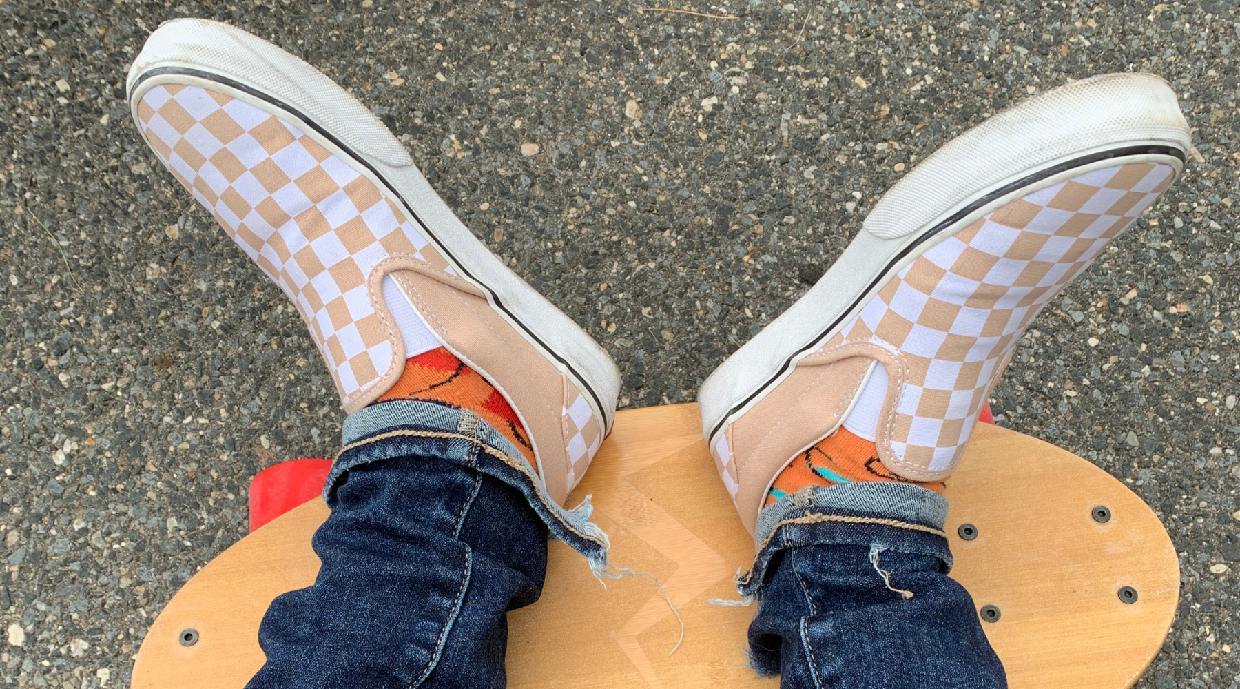 Closeup of two feet wearing checkered Vans shoes resting on the deck of an Eggboard mini cruiser skateboard in a park, highlighting the comfortable and stylish riding experience