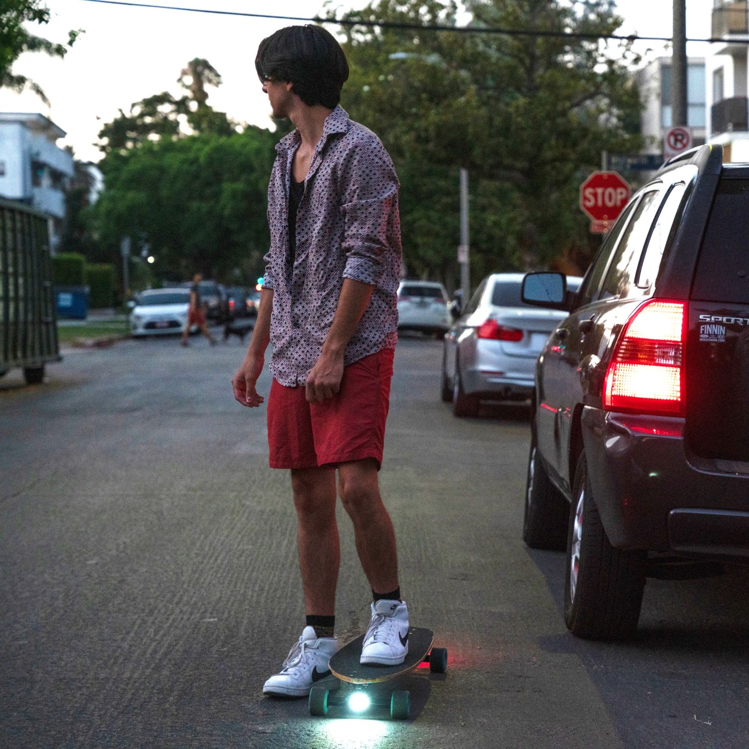 A guy on a road with his cruiser skateboard equipped with Eggboard LED lights turned on, looking back and ready to ride, showcasing enhanced visibility for nighttime skating.