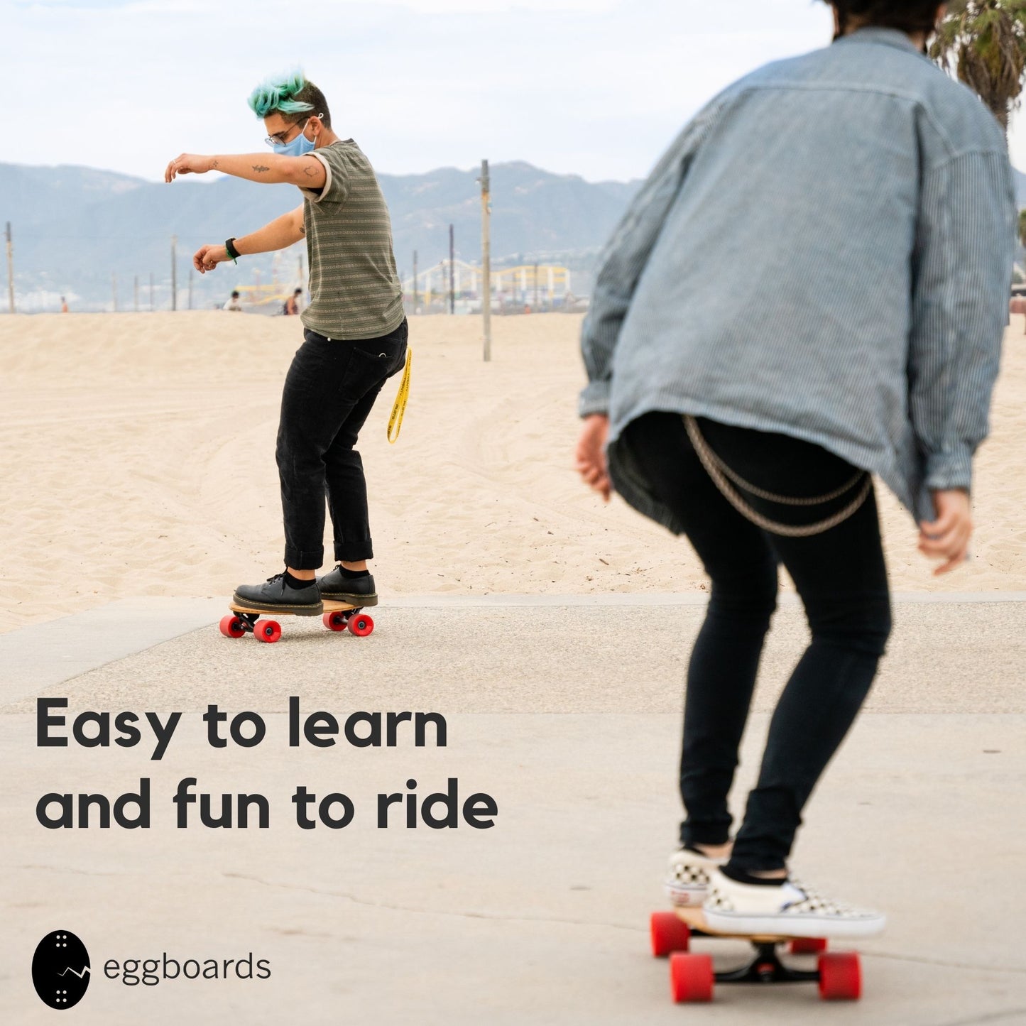 A guy and a girl riding Eggboard mini cruiser skateboards by the beach in Santa Monica, California, on a foggy day. The image features an overlay that says "Easy to learn and fun to ride"